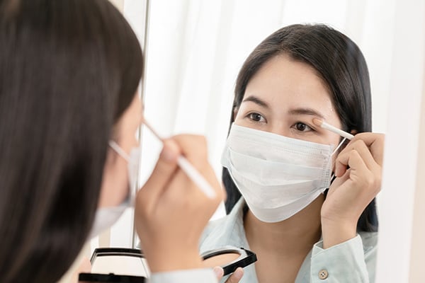 woman wearing mask applying eyeshadow - Learn more about cosmetic trends