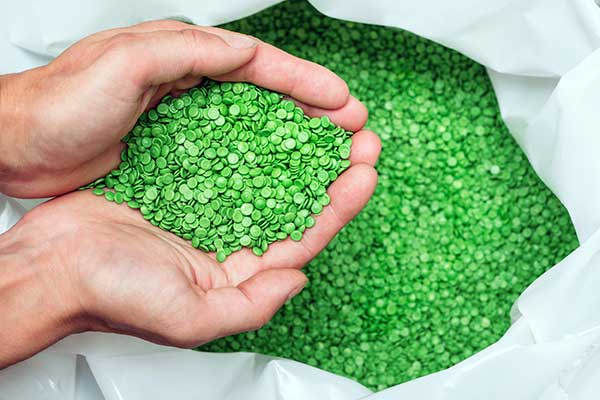 Hands scooping up green biodegradable plastic pellets